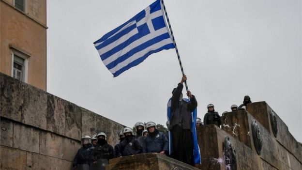 An Orthodox monk waves a Greek national flag next to riot police