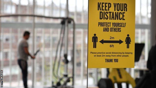 A sign reminds gym users of social distancing protocols as they exercise on the machines at Kensington Leisure Centre in London