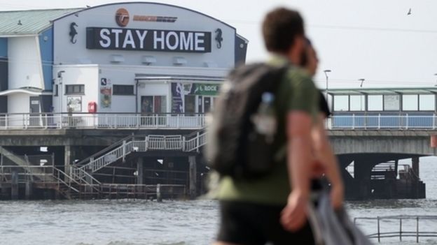People walk past a sign saying 'Stay Home' projected from Bournemouth pier