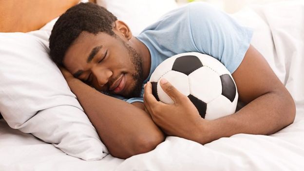 Un hombre duerme abrazado a un balón de fútbol.