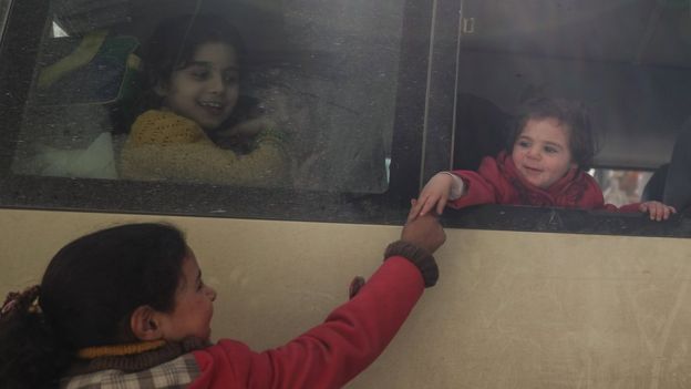 A girl shakes hand with a friend sitting in a bus during the second day of medical evacuations from the besieged rebel-held Eastern Ghouta (14 March 2018)