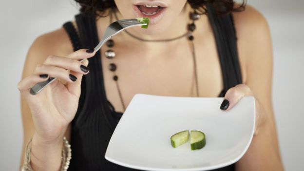 Una mujer comiendo una rodaja de pepinillo partida en cuatro