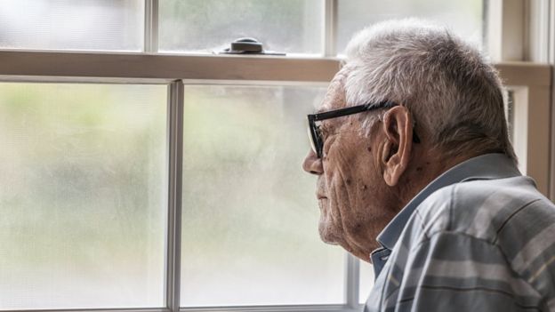 Anciano mirando a través de una ventana.
