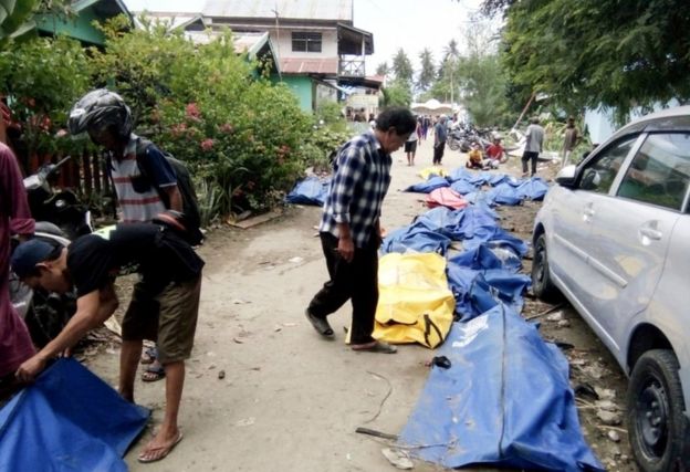 Locals check bodybags as they search for their families in a Palu street