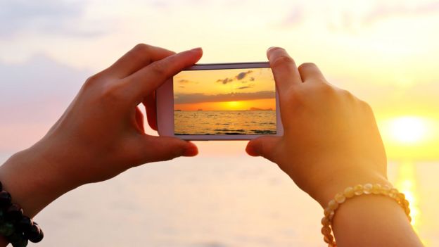 Una chica sosteniendo un celular mientras toma una foto del mar