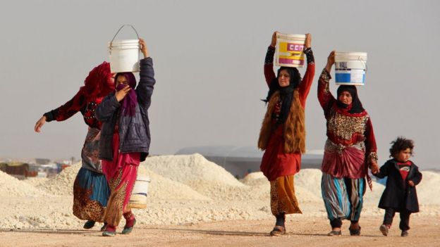 Syrian women displaced carrying water