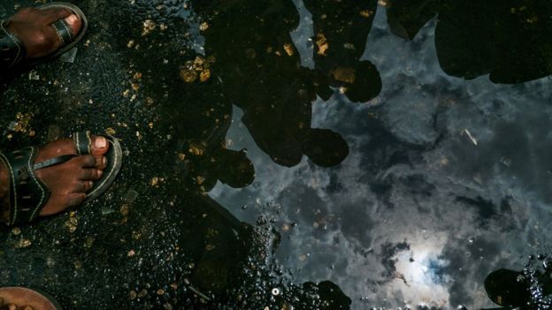 People use a puddle of water to look at a annular solar eclipse in the sky of in Dar es Salaam on September 1, 2016.