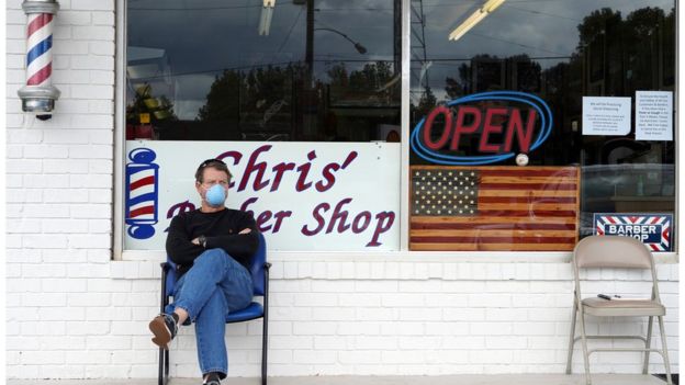 a man in a mask sits in front of his barber shop
