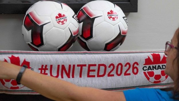 Una mujer junto a dos balones y una bufanda de la candidatura de Canadá al Mundial