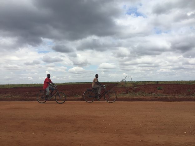 Chicos montando en bicicleta frente a terrenos baldíos.