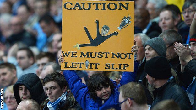 A sign is held up with a mocked-up image of Steven Gerrard and the words 'Caution - we must not let it slip'