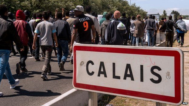 Migrants walk past a "Calais" sign