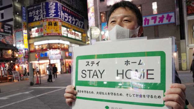 Funcionario del gobierno municipal de Tokio con un carte de "quédense en casa".
