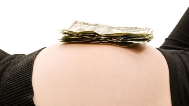 Barriga de embarazada con billetes de dólares encima.