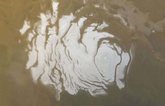 A white layer of ice in a swirl shape, on the dusty landscape of Mars