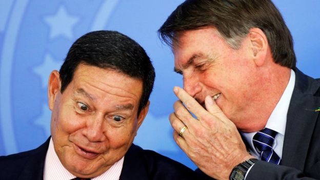 Tapando a boca, Bolsonaro fala no ouvido de Hamilton Mourão