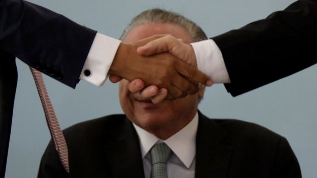 Aperto de mão cobre o rosto do presidente Michel Temer