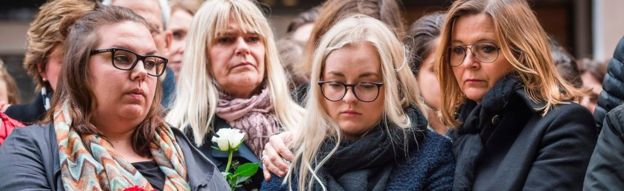 People react during a minute of silence to commemorate the victims of Friday's attack at a makeshift memorial near the site where a truck drove into Ahlens department store in Stockholm