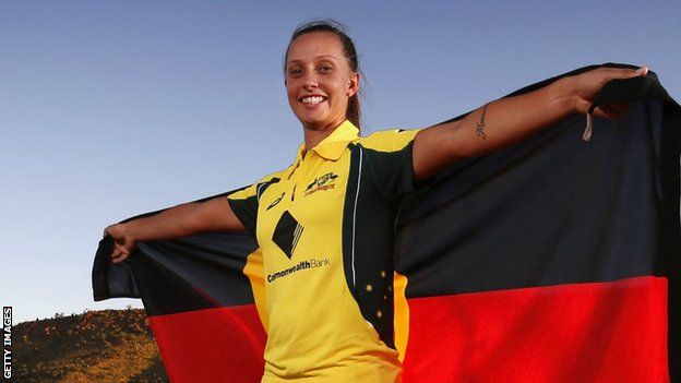 Ash Gardner in Australia kit, holding up a giant Australian Aboriginal flag