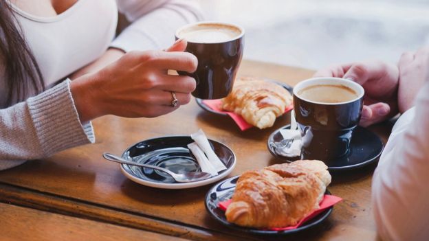 Duas pessoas bebeno café e comendo croissants