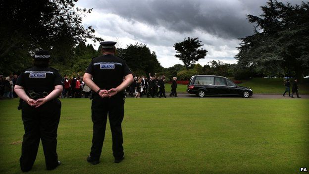 Police officers look on as mourners follow the coffin of Lamara Bell