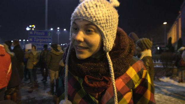 Tania, a young protester wearing a wool hat speaks to the BBC in the street