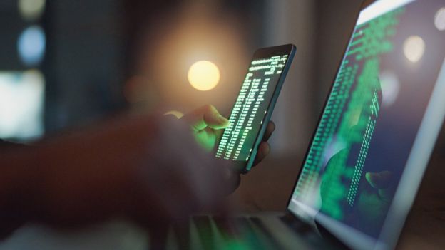 Telas de celular e de laptop mostram códigos, indicando ação de hacker