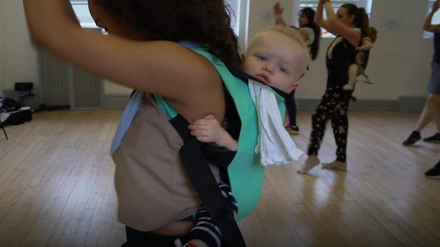 A mother with a baby in a sling during a dance class
