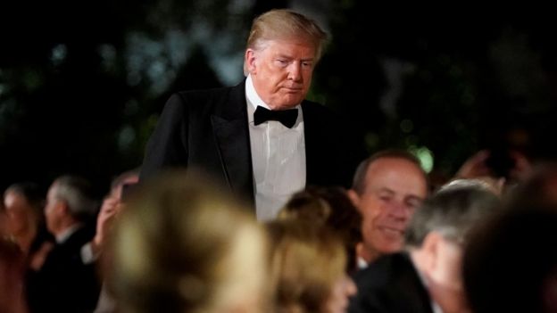 Trump em pé, em meio a outras pessoas sentadas, durante evento de gala