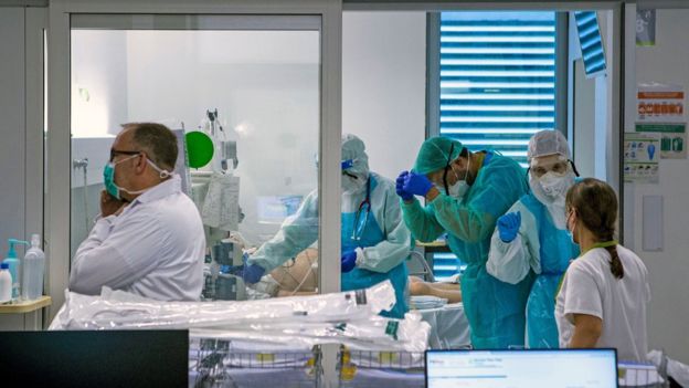 Médicos com equipamentos de proteção atendem paciente, cujo rosto não é visível, em cama de hospital na espanha