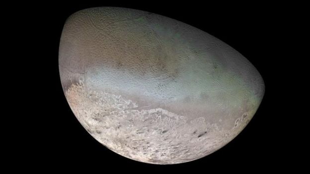 Half the face of Triton, its blue-green surface is mottled like a cantaloupe