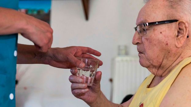 Un ayudante acerca un vaso de agua a un hombre mayor