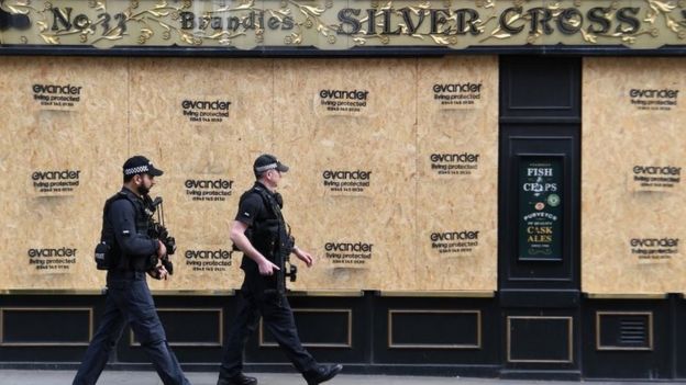 Two police officers walk past a boarded-up pub