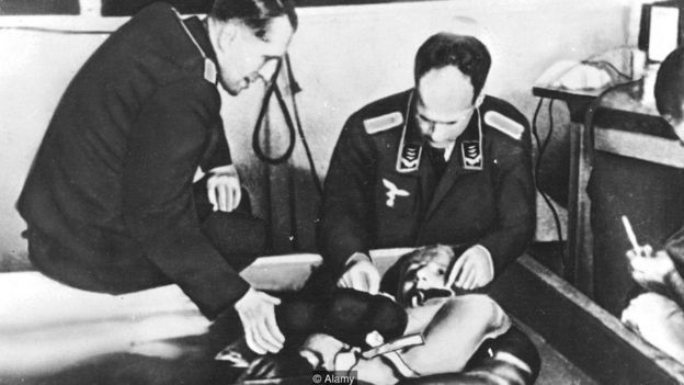 Em foto em preto e branco, dois médicos nazistas fazem experimento em homem