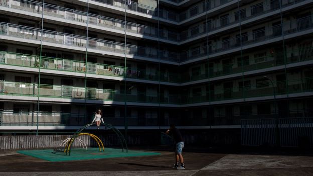 A woman poses for photographs in front of a public housing estate in Hong Kong on May 14, 2015.