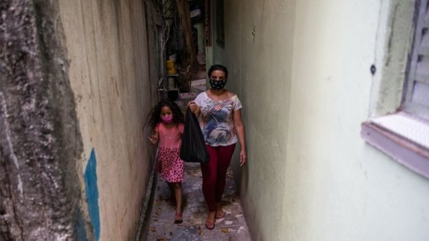 Mulher e menina caminham em favela em São Paulo