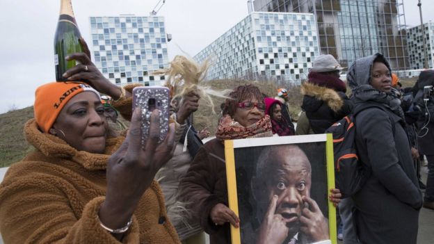 Supporters of Laurent Gbagbo rally outside the ICC, holding up a photo of him and a bottle of champagne