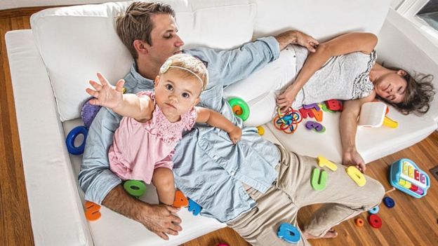 Dos padres recostados en un sofá con un bebé
