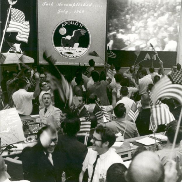Controladores de vuelo en el centro de control de Apolo 11 celebrando con banderas de Estados Unidos