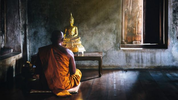 Monge ora diante de estátua de Buda
