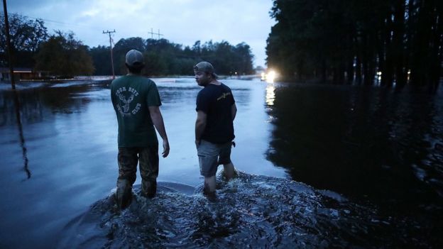 Two men stand in knee deep waters on a highway in Kinson, North Carolina