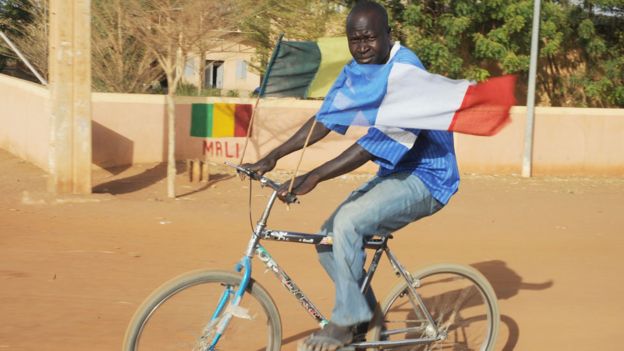 A man in Mali with Malian and French flags flying from his bicycle