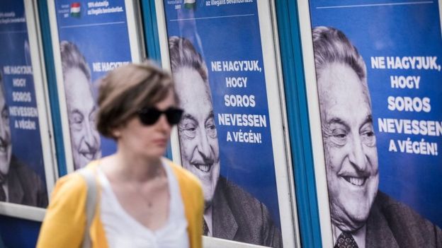 A woman walks past a wall of Soros posters