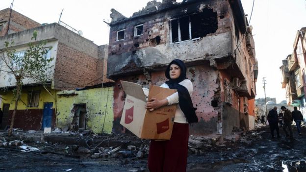 Diyarbakır'ın Sur ilçesinde 11 Aralık 2015'te çekilen bu fotoğrafta çatışmalarda yıkılan evlerde kurşun izleri görülüyor. Bir kadın da koli içindeki eşyalarını taşıyor.