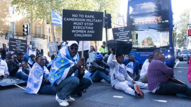 Manifestantes pro Ambazonia sentados en una calle de Londres deteniendo el tráfico.