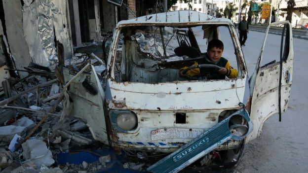 Niño juega dentro de un auto destrozado en Siria