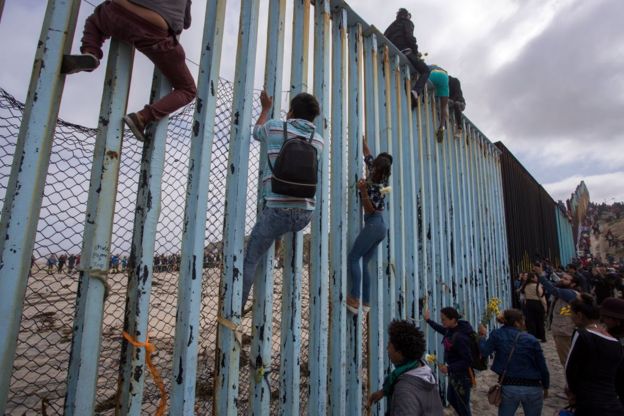 Personas sobre la reja que marca la frontera entre México y Estados Unidos