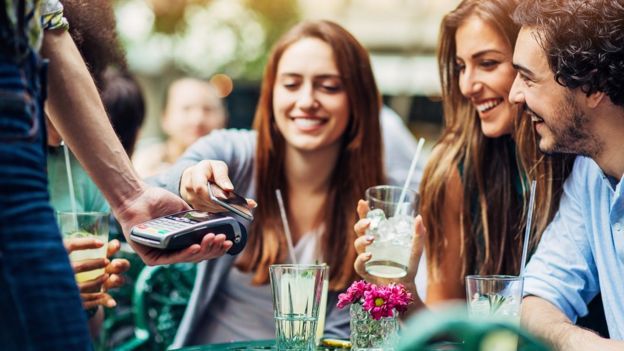 A woman uses her smartphone to pay for a meal at a restaurant with friends