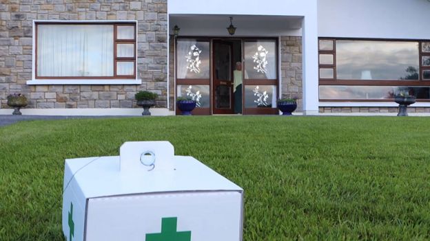 A package with a pharmacy logo on it is seen on the grass in a front garden