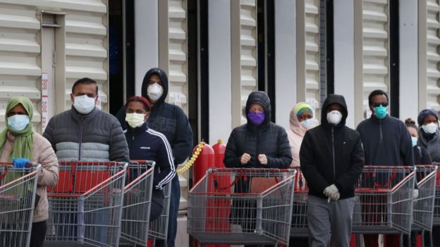 Uma fila de compradores, todos usando máscaras faciais